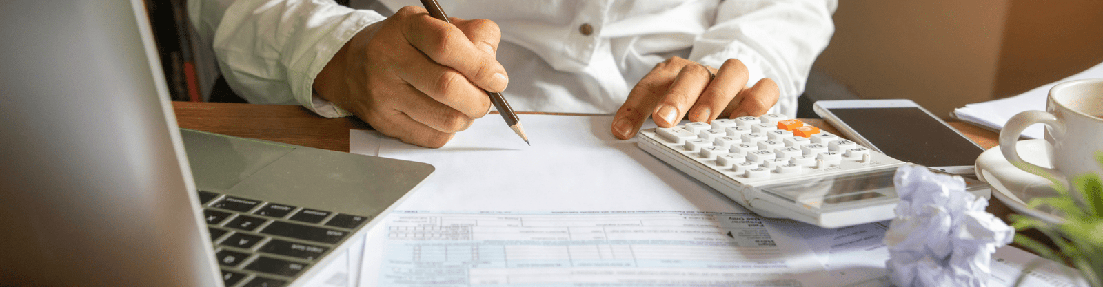 Person reviewing financial documents with a calculator and laptop, symbolizing tax preparation or financial planning.